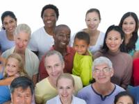 A group of young and old people of many ethnicities looking up at the viewer and smiling.