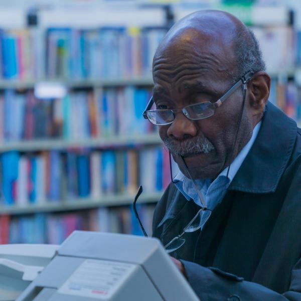 A man operates a scanning machine in front of library shelves.