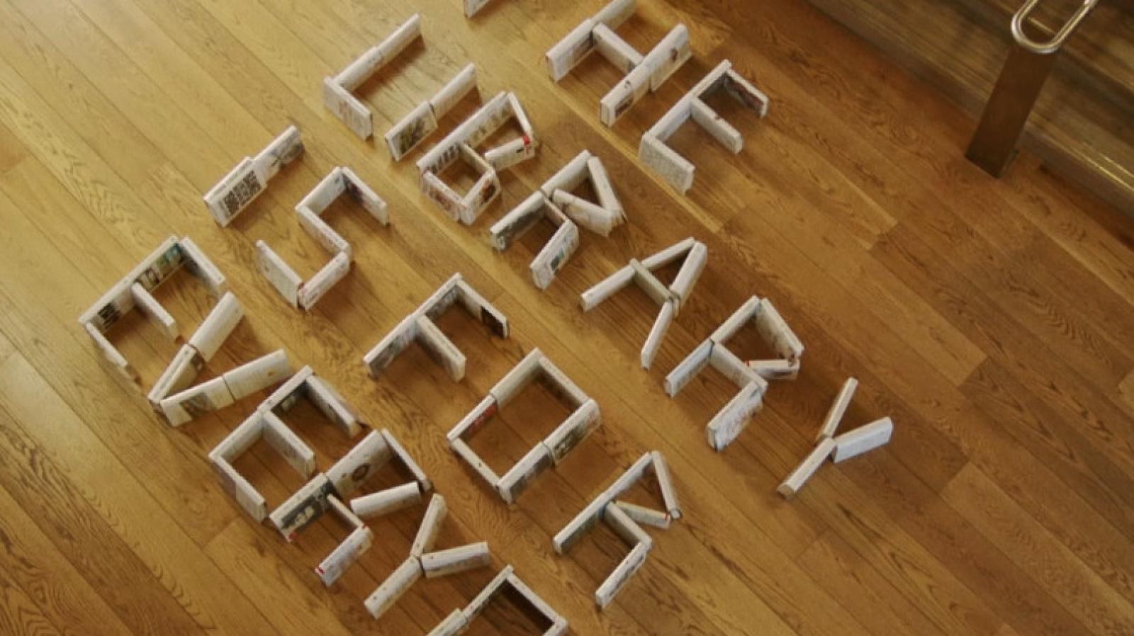 Books arranged on a wooden library floor to spell "The Library is for Everyone"